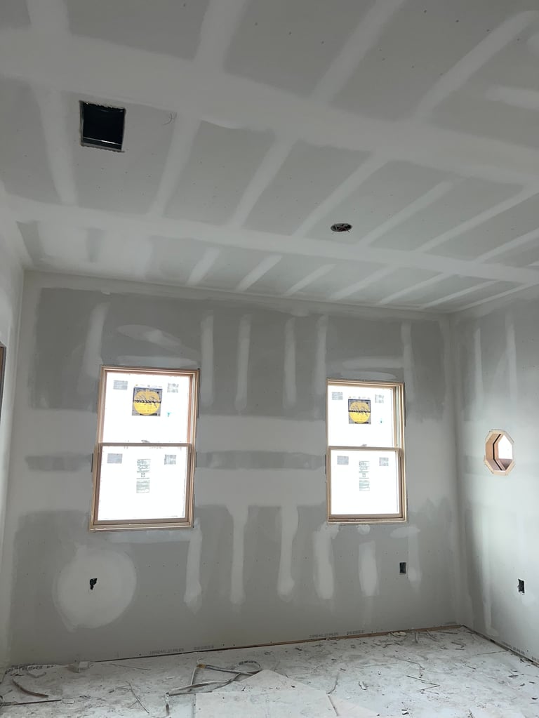 Unfinished drywall room with two windows, ceiling fixtures, and protective covering on walls during construction
