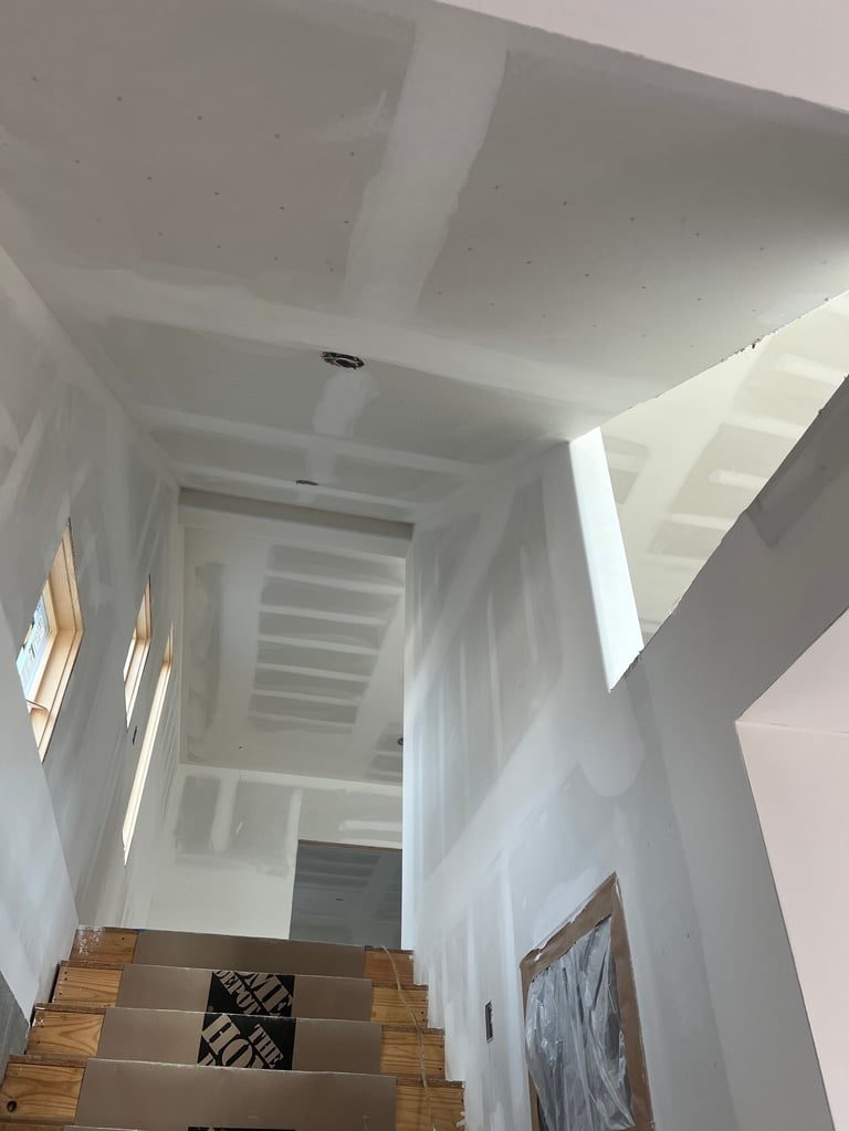 Interior view of a modern staircase with white drywall, wooden steps, and recessed ceiling details during construction or renovation
