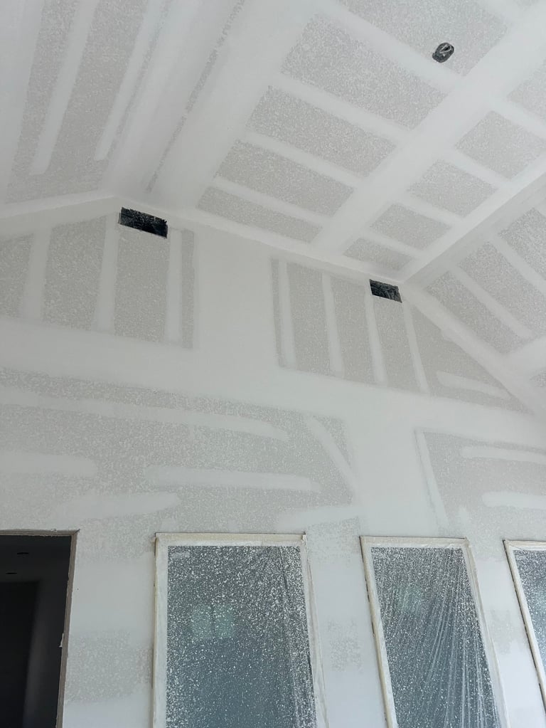 Interior room under construction with white drywall ceiling, recessed lights, and covered windows during renovation